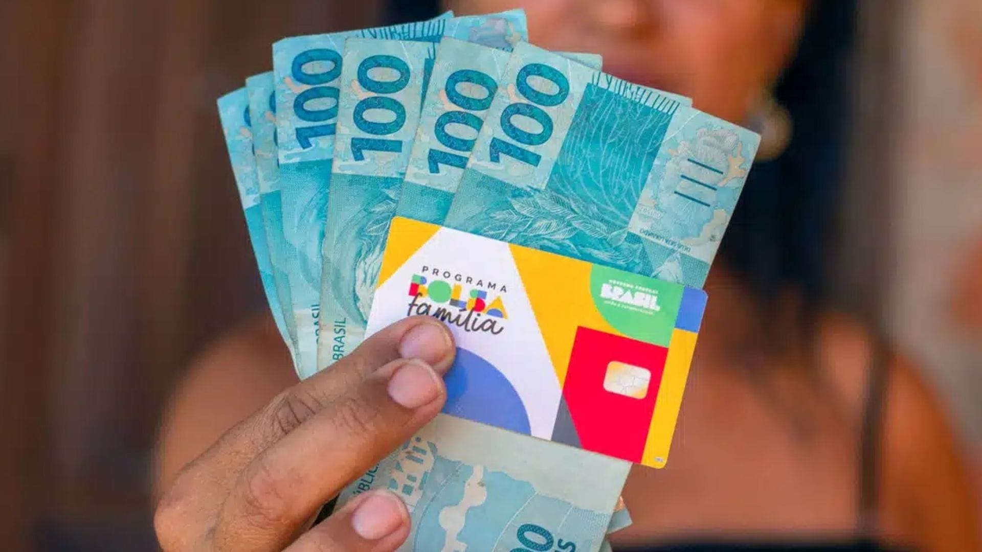 Mulher segurando o cartão do Bolsa Família com valor disponível para saque